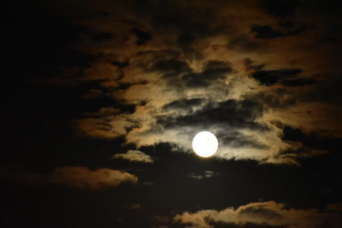 暗い夜空で雲を照らす満月